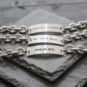 Three silver stainless steel inspirational bracelets on slate with motivational quotes