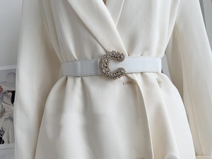 Detail of white leather belt with gold C-shaped buckle featuring sparkling rhinestones