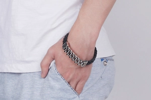 Close-up of men's stainless steel curb link bracelet with black woven leather on wrist