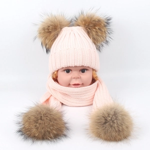 Detail of pink knitted baby hat and scarf set featuring four large fluffy brown fur pom-poms
