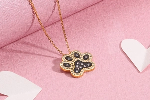 Detail of gold paw print pendant with black filling and sparkling crystals on pink background