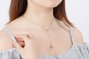 Detail view of a silver Y-shaped stainless steel necklace with a pink pearl pendant on a model