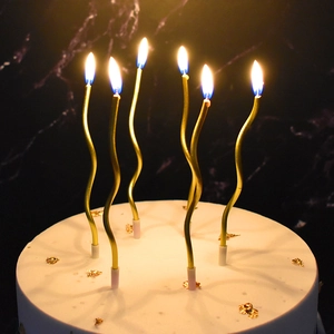 Set of six gold wavy spiral birthday candles burning on a cake with pink holders