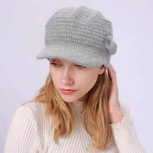 Detail einer grauen Strickmütze mit Schirm und seitlichem Bommel an einem Fotomodell