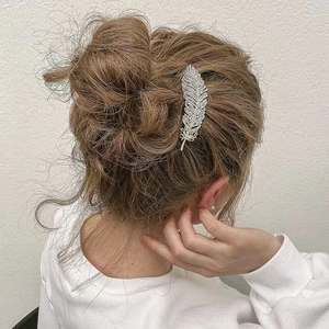 Elegant silver feather hair clip with rhinestones worn by a model in brown hair