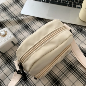 Top view detail of creamy white nylon crossbody bag showing the double zipper structure