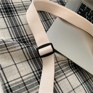 Detail of adjustable off-white woven strap with a black plastic buckle on a crossbody bag