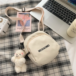 Detail of cream nylon crossbody bag featuring a plush bear charm and black text logo