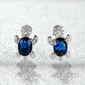 Macro shot of sea turtle stud earrings featuring deep blue zircon and silver metal