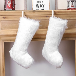 Two white fluffy plush Christmas stockings hanging on a wooden mantel with festive decor
