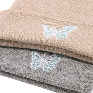Detailed view of butterfly embroidery on knitted beanies in beige and light grey colors