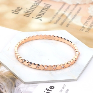 Close-up of rose gold hexagonal bangle with micro-set zircons on a white stone display