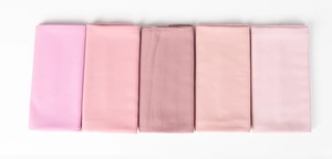 Detail of multi-shade pink pearl chiffon hijabs folded and neatly arranged on white background