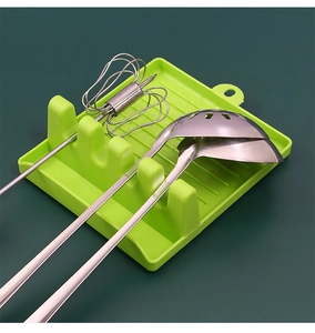Macro detail of a green kitchen utensil rest holding a spatula and whisk on a green surface
