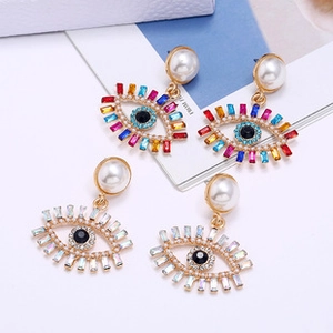 Detail of evil eye drop earrings with gold lashes and rectangle crystals on white card