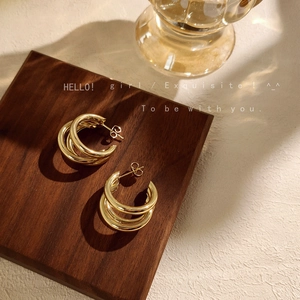 Detail view of triple-layered gold-plated hoop earrings on a minimalist wooden display