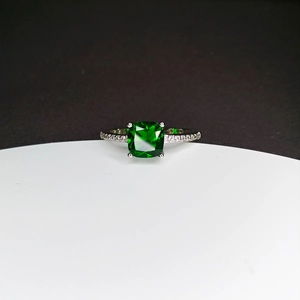 Macro detail of square cut green gemstone set in silver band with accent diamonds