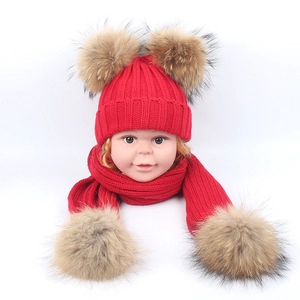 Detail of red cable-knit children's hat and scarf set with large double faux fur pom-poms