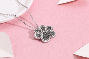 Macro detail of silver dog paw pendant with sparkling rhinestones on a pink background