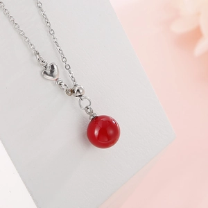 Silver chain necklace with heart charm and large polished red sphere on white stand