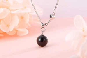 Detail of silver chain necklace with black bead pendant and heart accent on pink background