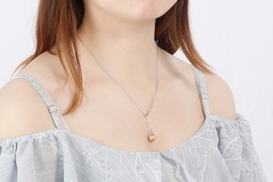 Close-up of elegant silver necklace featuring a golden pearl pendant worn by a model