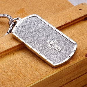 Close-up of matte silver rectangle pendant with inlaid cross on a wooden background