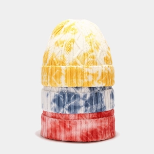 Vertical stack of three tie-dye knitted beanies in yellow, blue, and red patterns