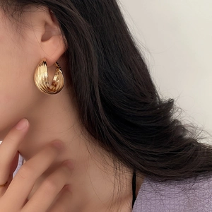 Close-up of golden multi-layered twisted hoop earrings worn by a female model