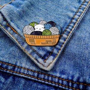Detail of cute cat in yarn basket enamel pin pinned on a blue denim jacket pocket