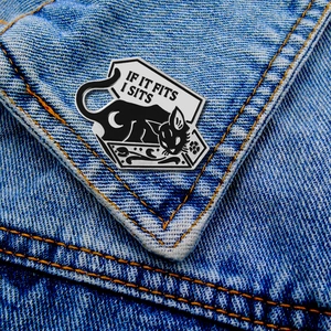 Detail of a black cat enamel pin with IF IT FITS I SITS text on denim jacket pocket