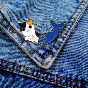 Detail of a cat mermaid enamel pin with gold metal edges pinned on a blue denim jacket
