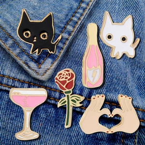 Set of 6 enamel pins with black cat, pink wine bottle, and rose on denim fabric background