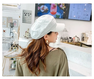 Side view of a white linen newsboy cap styled with gold hoop earrings in a cafe