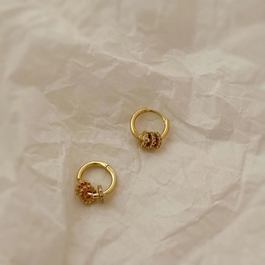 Boucles d'oreilles créoles dorées avec détail d'engrenage en zircone sur fond minimaliste