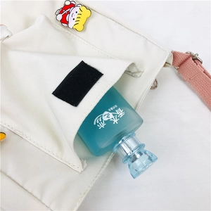 Détail du sac à bandoulière en toile blanche avec badge cartoon et flacon de parfum