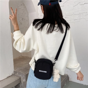 Detail view of small black canvas crossbody bag with white bear plush keychain and lettering
