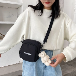 Detail of black nylon crossbody bag featuring a cute white teddy bear plush charm
