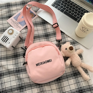 Detail of pink canvas crossbody bag with adjustable strap and decorative pendant on grid cloth