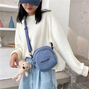 Detailed shot of a blue nylon crossbody bag with adjustable strap and plush bear charm