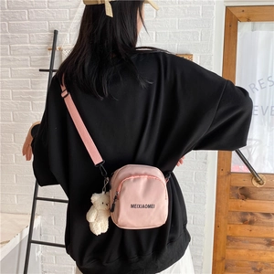 Pink nylon crossbody bag with cute bear pendant shown on model against a white brick wall