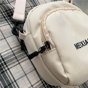 Detailed close-up of cream white nylon crossbody bag featuring black plastic hardware and strap
