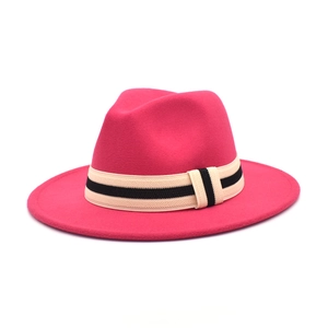 Detail of rose red fedora hat with a striped beige and black ribbon on white background