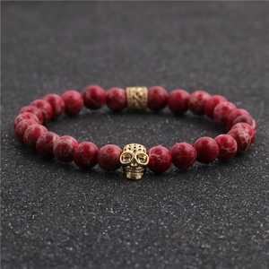 Red jasper stone bracelet with golden skull charm and hollow spacers on dark surface