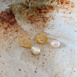 Detail of gold floral earring with baroque pearl drop on ceramic display base