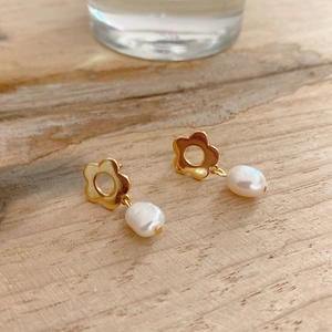 Detailed close-up of golden flower stud earring with a white baroque pearl on wood
