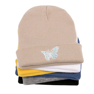Close-up of stacked knitted beanies featuring delicate butterfly embroidery on beige fabric