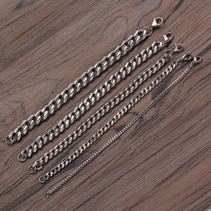 Macro shot of silver stainless steel Cuban link chains with lobster clasps on wood