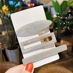Detailed view of three glittery silver-grey geometric hair clips with gold alloy bases