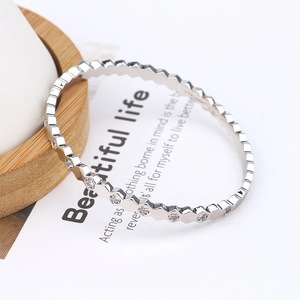 Detail of silver hexagonal bangle with pavé zircons on a white card with wooden base